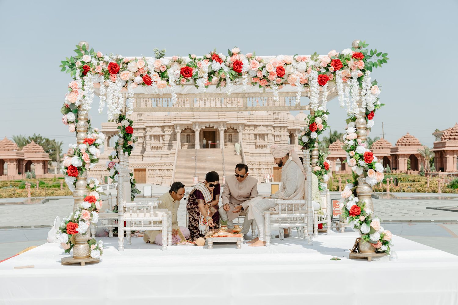 Outdoor wedding venue decorated with red and pink roses against stone architecture.
