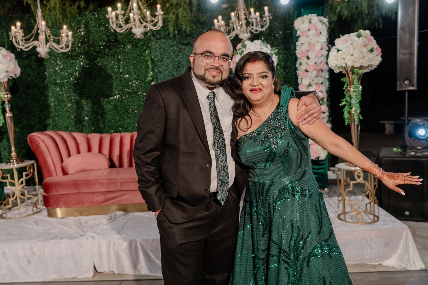 Formal gathering with guests in evening attire posing near decorative floral arrangements and chandeliers.