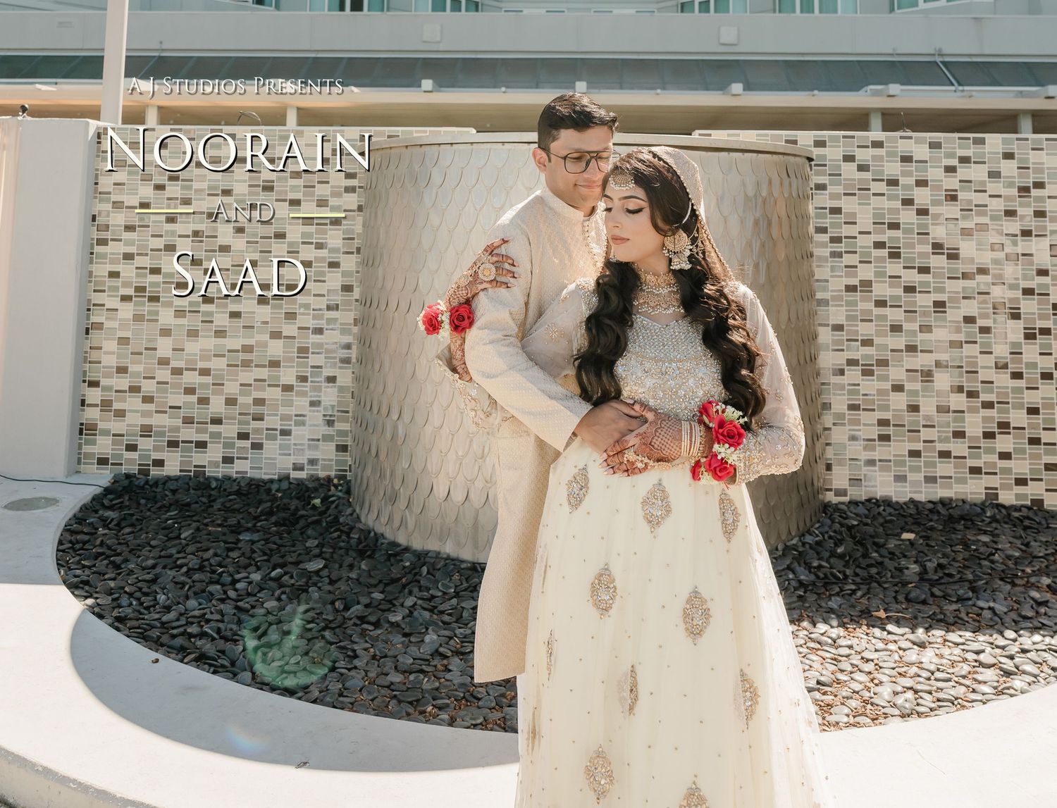 A couple in traditional cream-colored South Asian wedding attire poses together against a modern architectural backdrop.