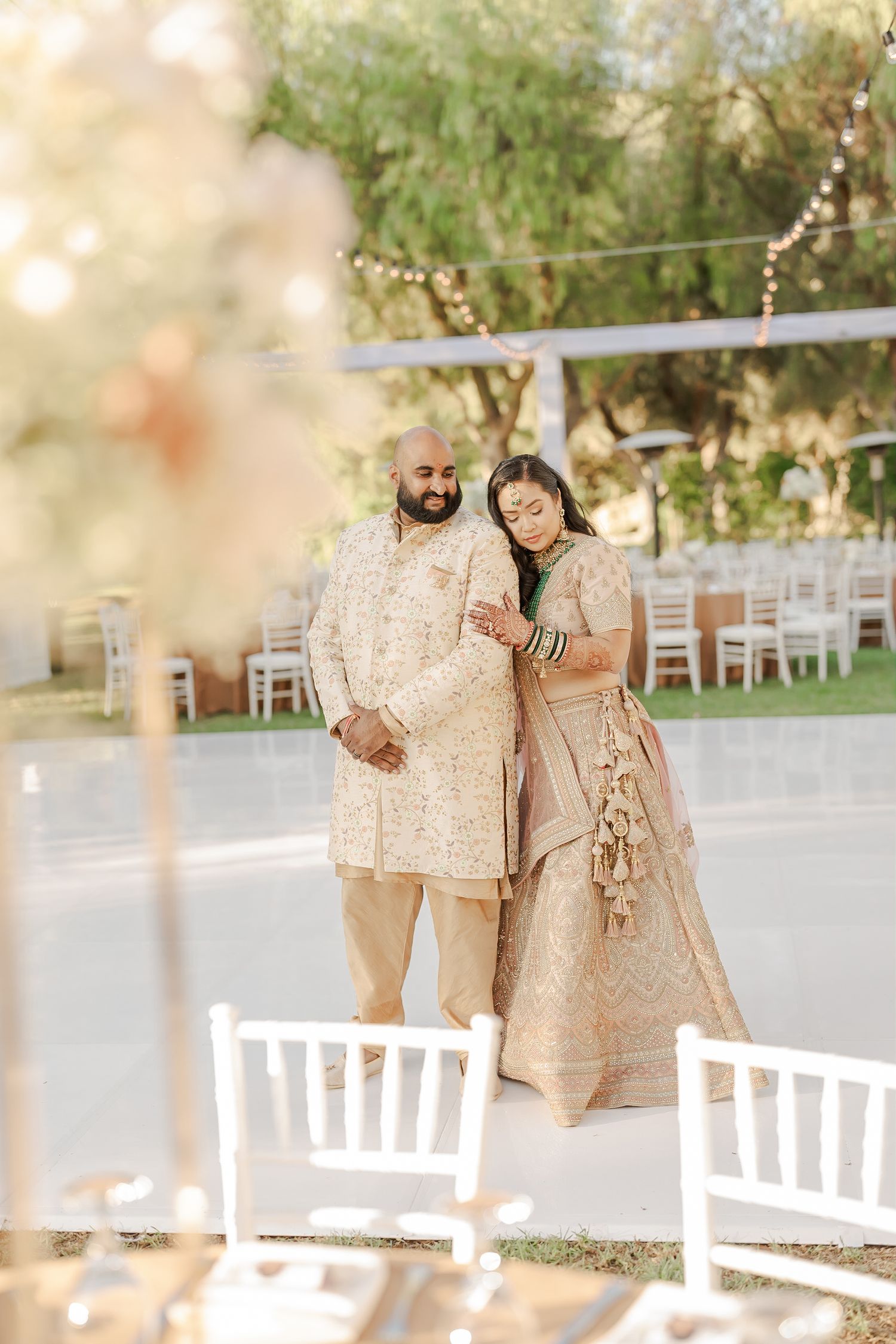 A couple shares a joyful moment together at an outdoor wedding venue with white chairs and natural lighting.
