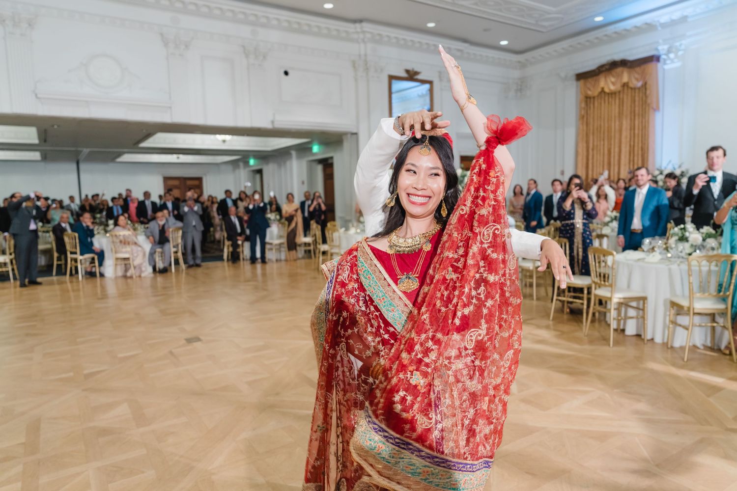 Wedding guests dance in a line formation across an elegant ballroom floor.