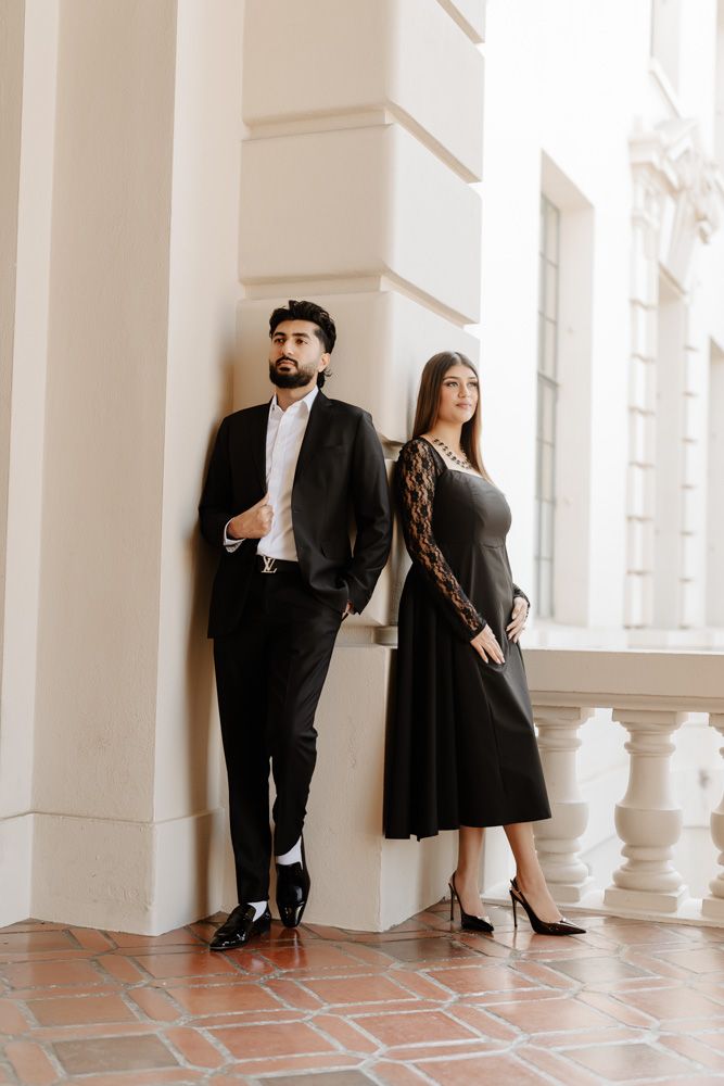 Stylish couple in black formal wear leaning against white column at Pasadena City Hall.