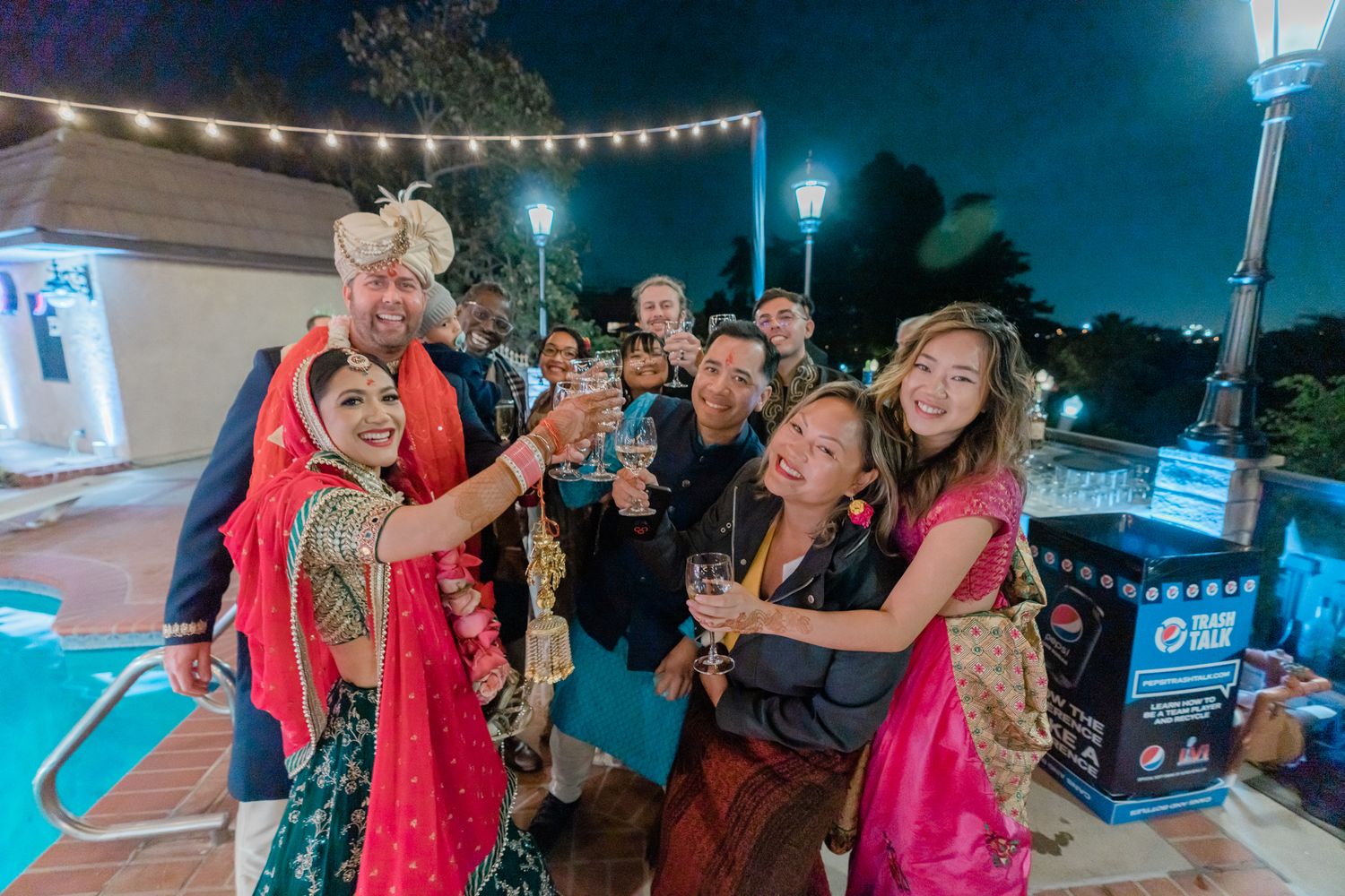 A group of people dance and celebrate at an outdoor nighttime party with string lights overhead.
