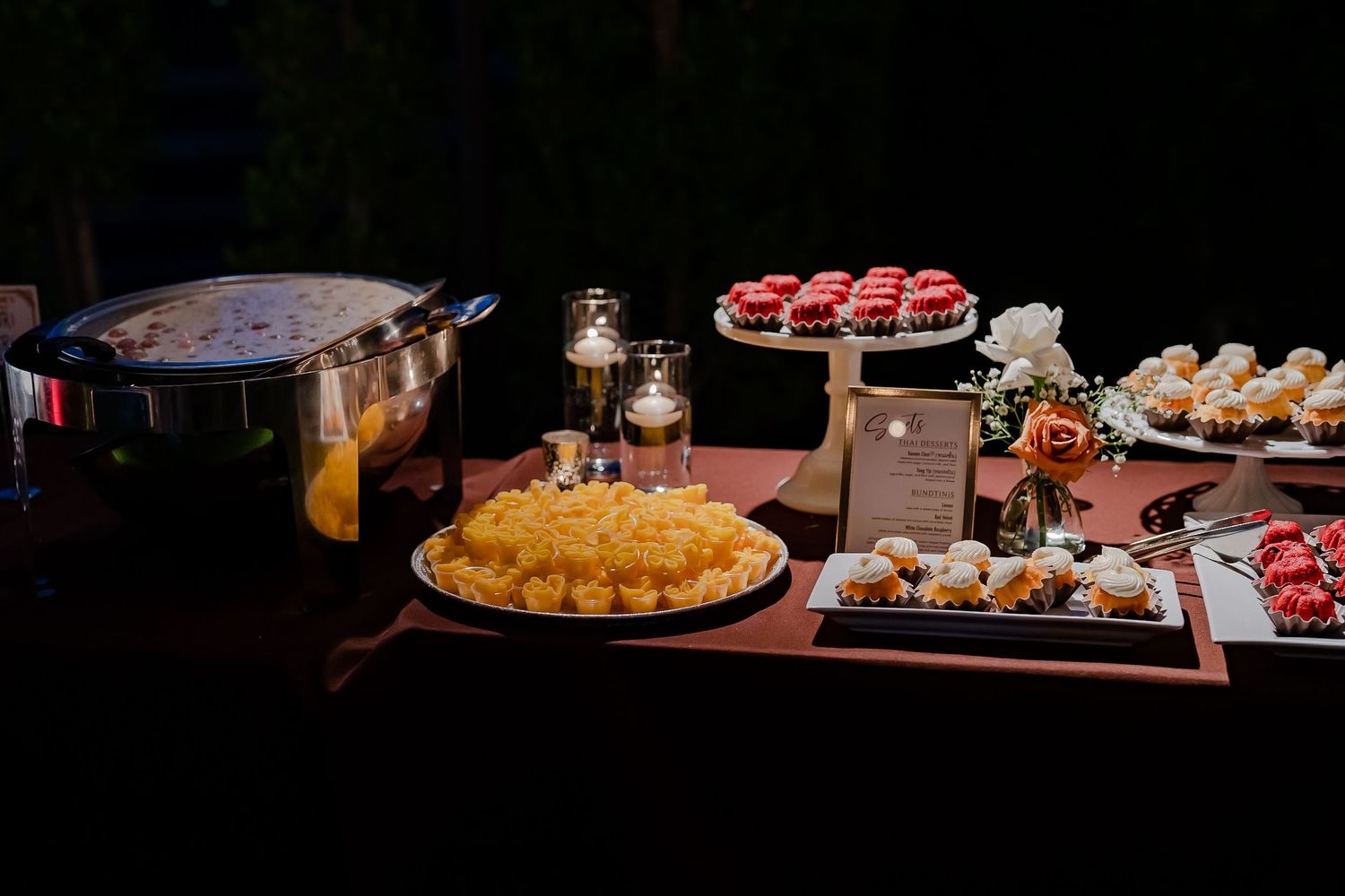 An elegant banquet table displays various appetizers and desserts with decorative lighting and floral arrangements.
