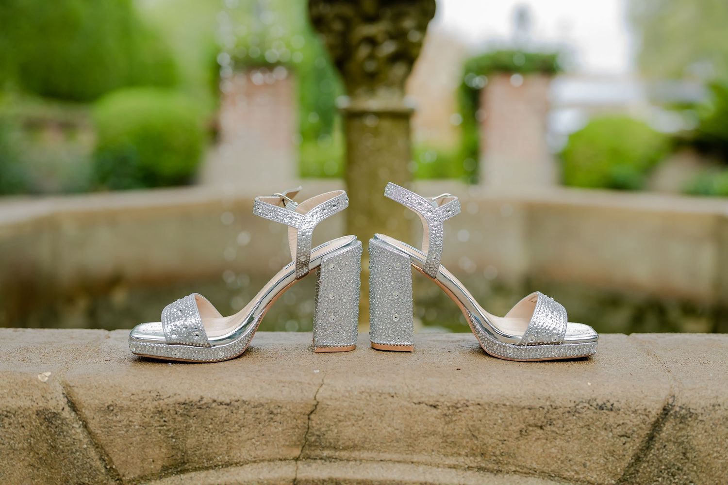 Wedding rings displayed on a stone ledge with blurred green garden scenery in the background.