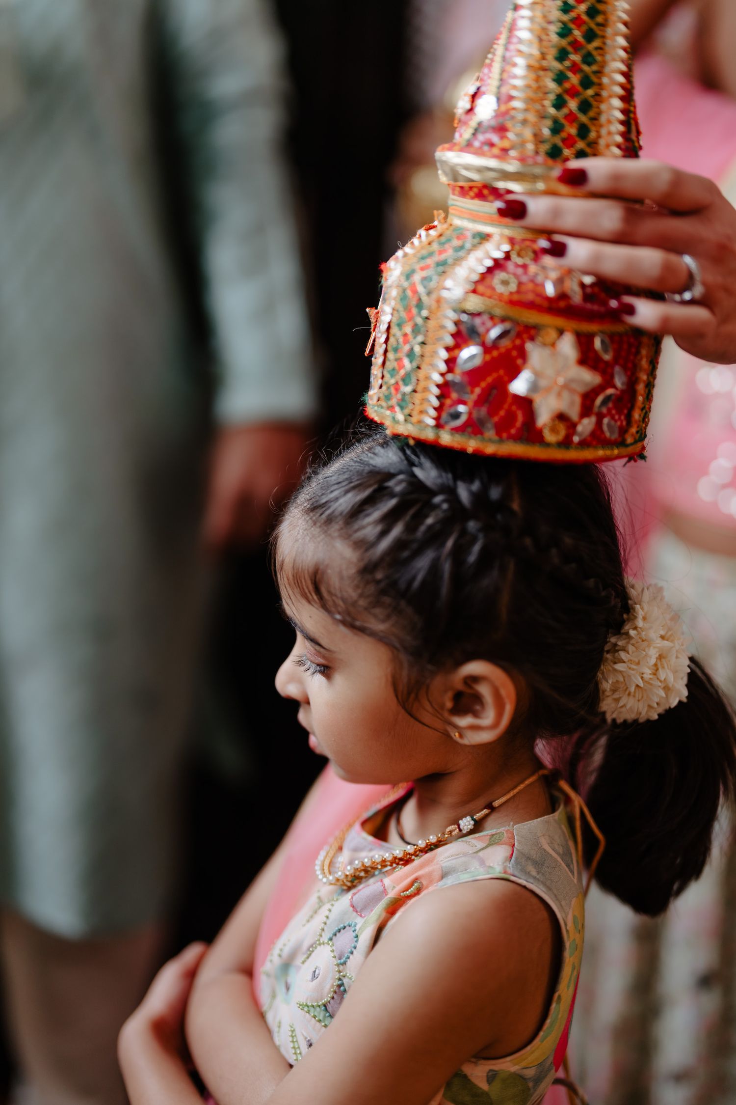 Young child wearing an ornate traditional red and gold crown during a cultural celebration.