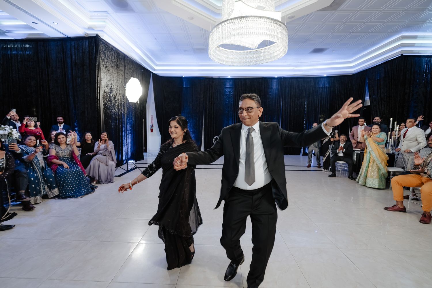 Wedding guests dancing and celebrating on an illuminated ballroom floor.