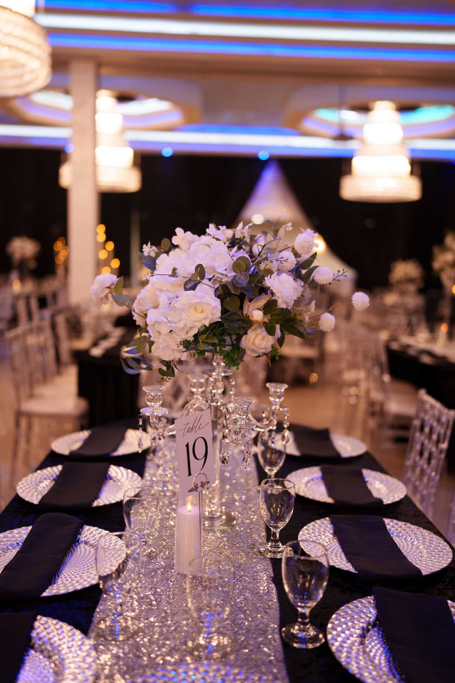 Elegant wedding reception tables decorated with white floral centerpieces, navy napkins and sparkling crystal glassware.