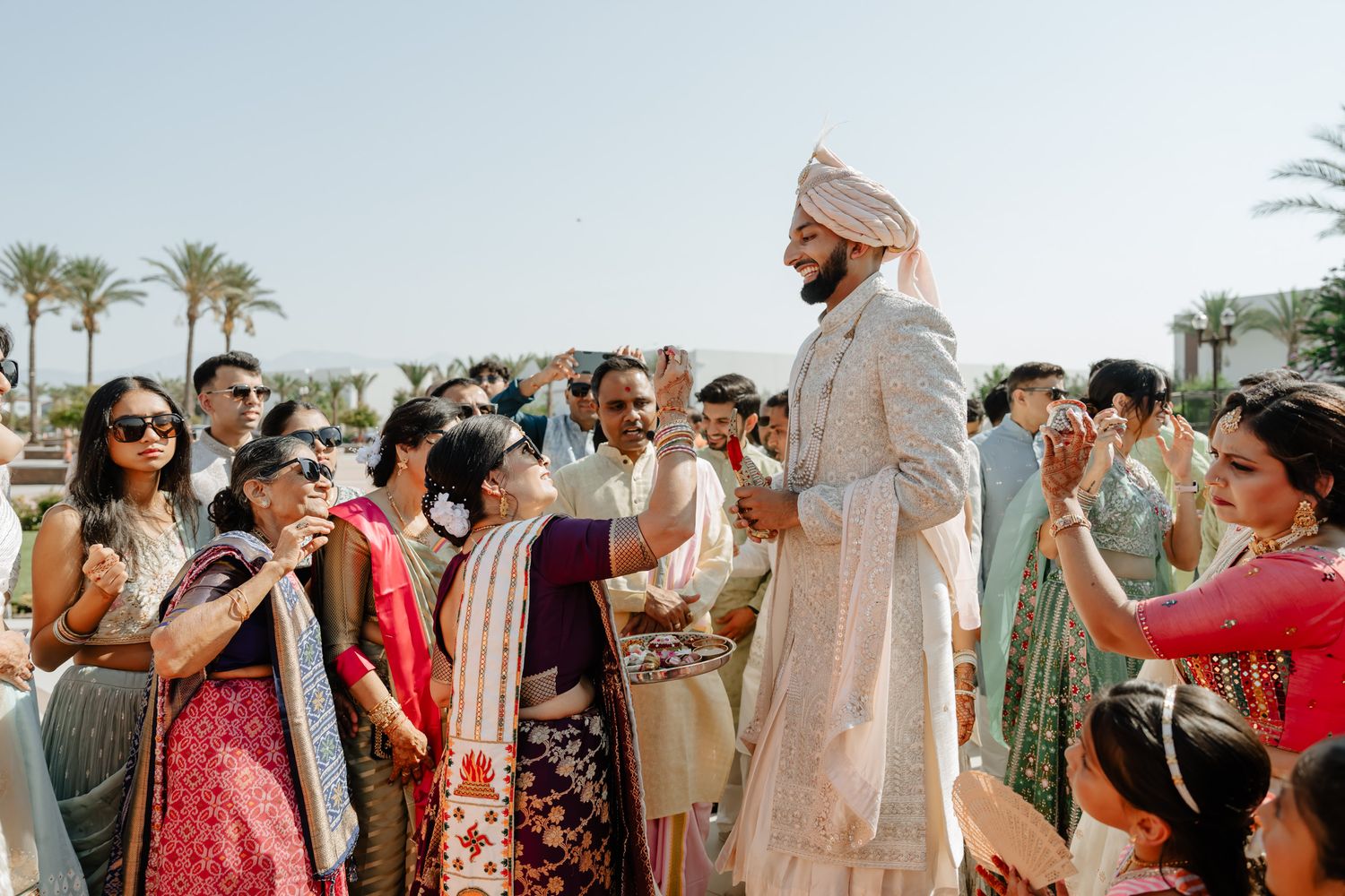 Wedding guests mingling and taking photos at an outdoor celebration with palm trees in the background.