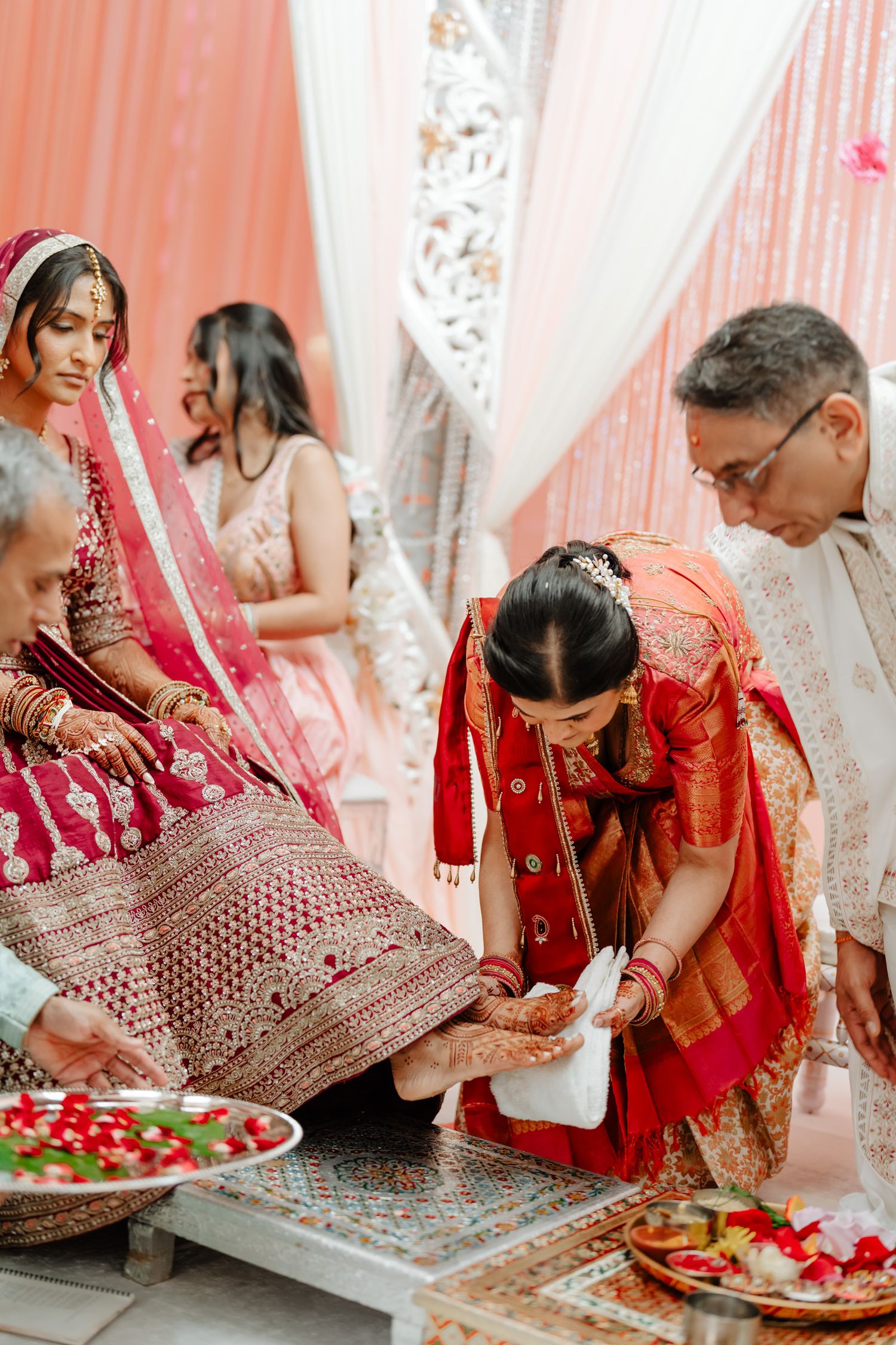 Traditional Indian wedding ritual showing guests seated on floor with decorative plates and red ceremonial attire.