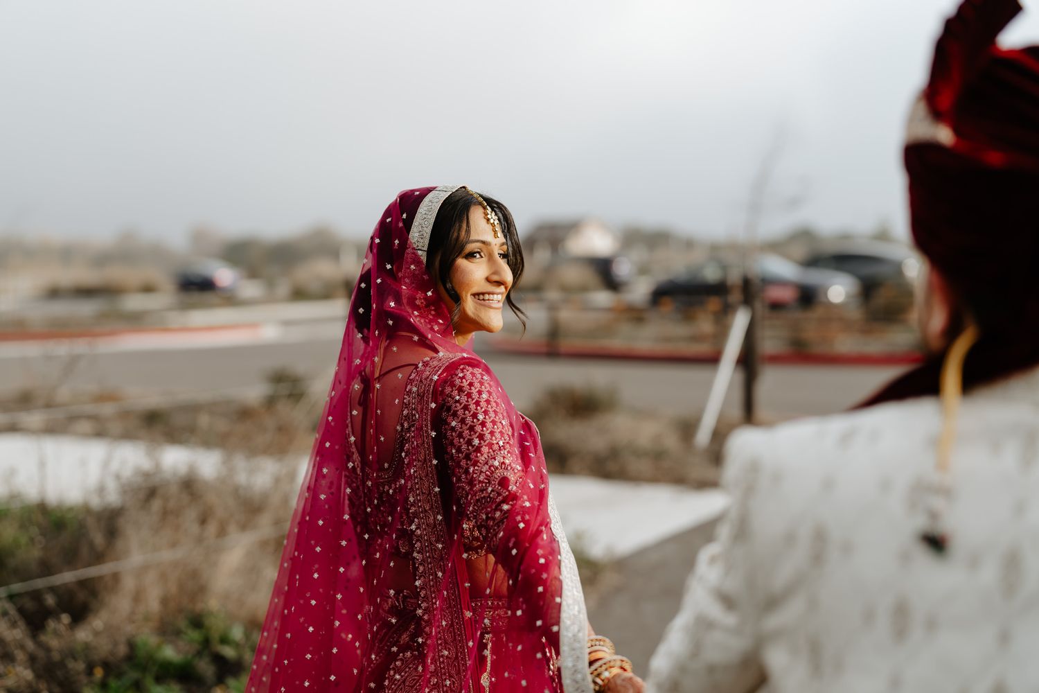 A person wearing a deep red embroidered dress stands in an outdoor setting with a misty mountain landscape in the background.