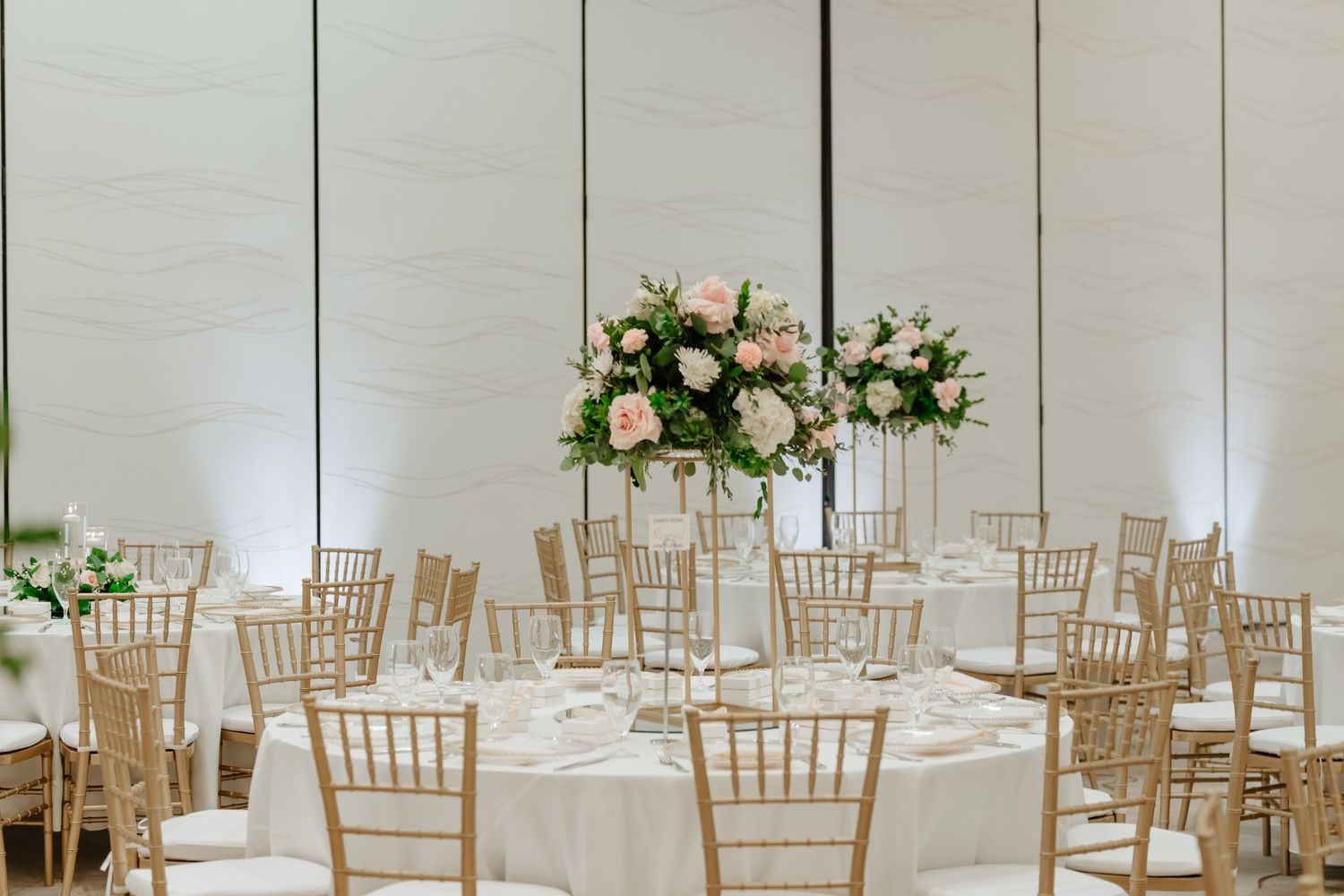 Elegant wedding reception venue with white linens, chiavari chairs and floral centerpieces in a light-filled space.
