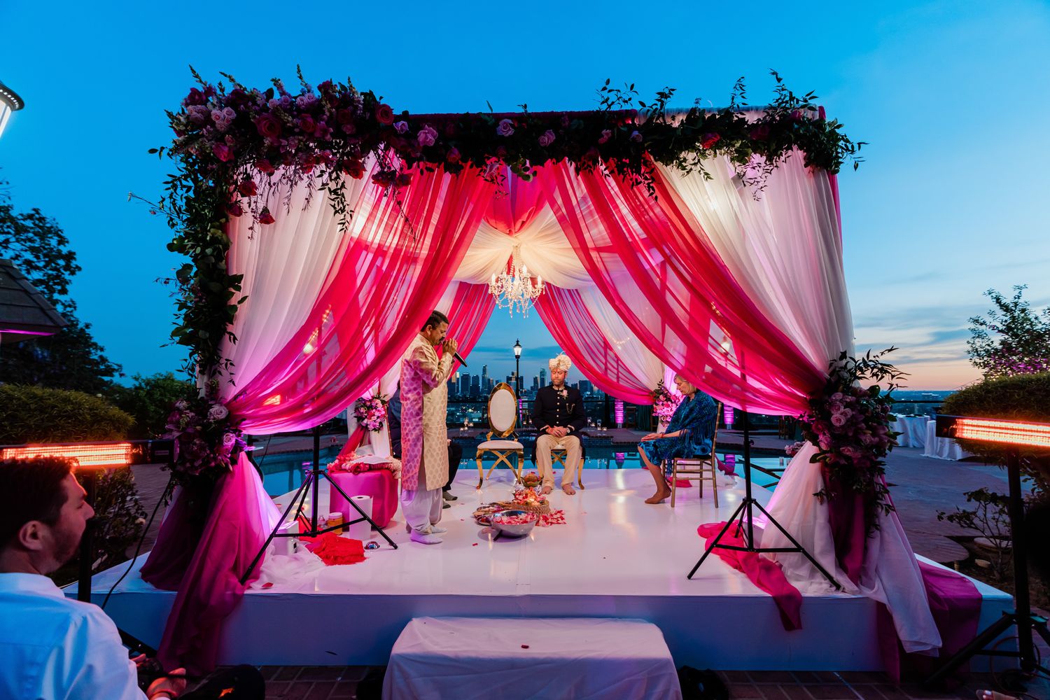 Outdoor wedding venue decorated with pink drapes and floral arrangements under blue sky.