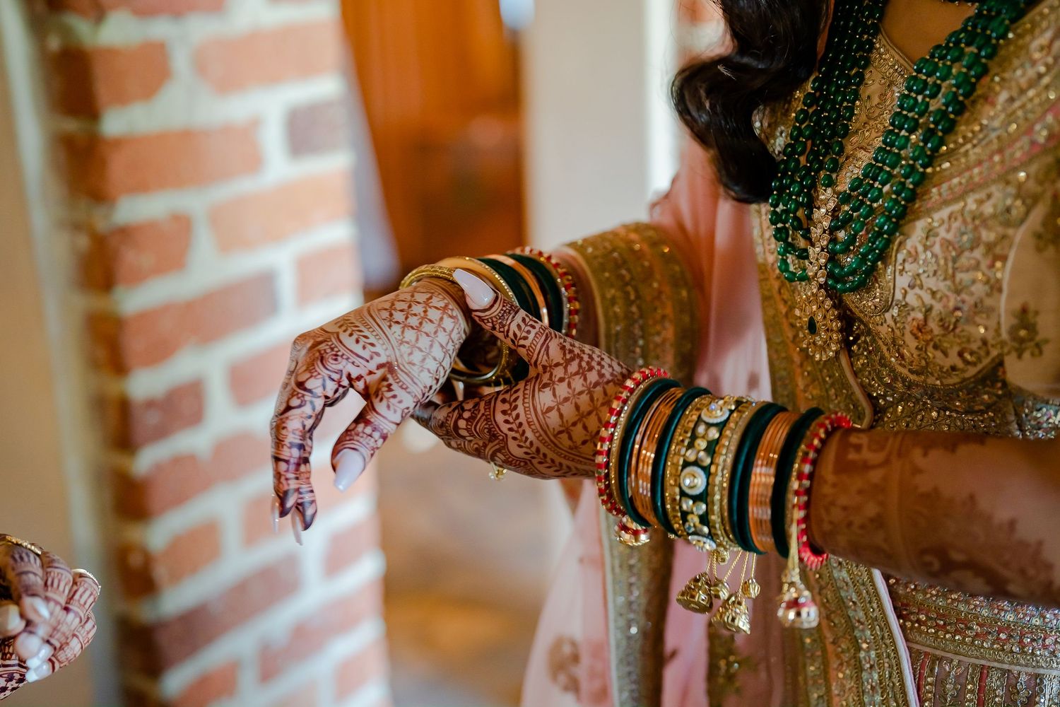 Close-up details of traditional Indian wedding jewelry and henna adorned hands against a brick wall background.