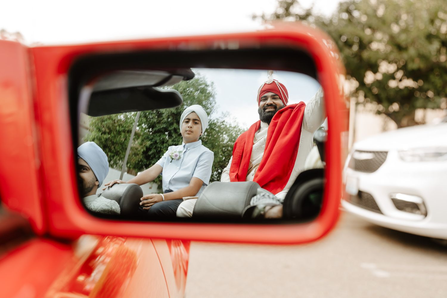 Red car frames a candid moment during an outdoor celebration.