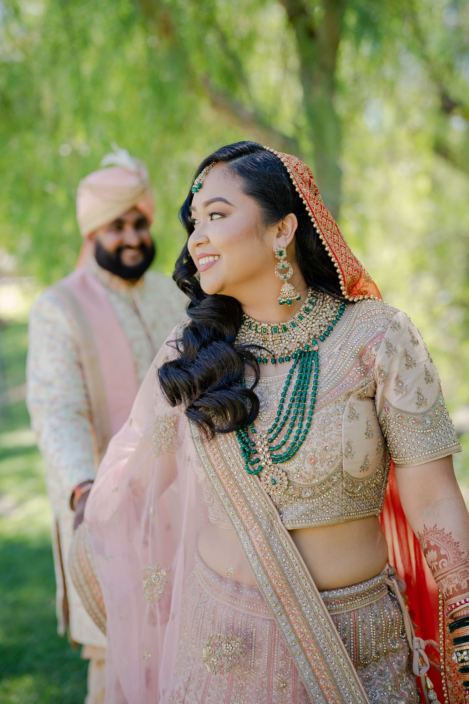 Beautiful South Asian wedding attire featuring intricate embroidered lehenga, turquoise jewelry and soft pink dupatta in outdoor setting.