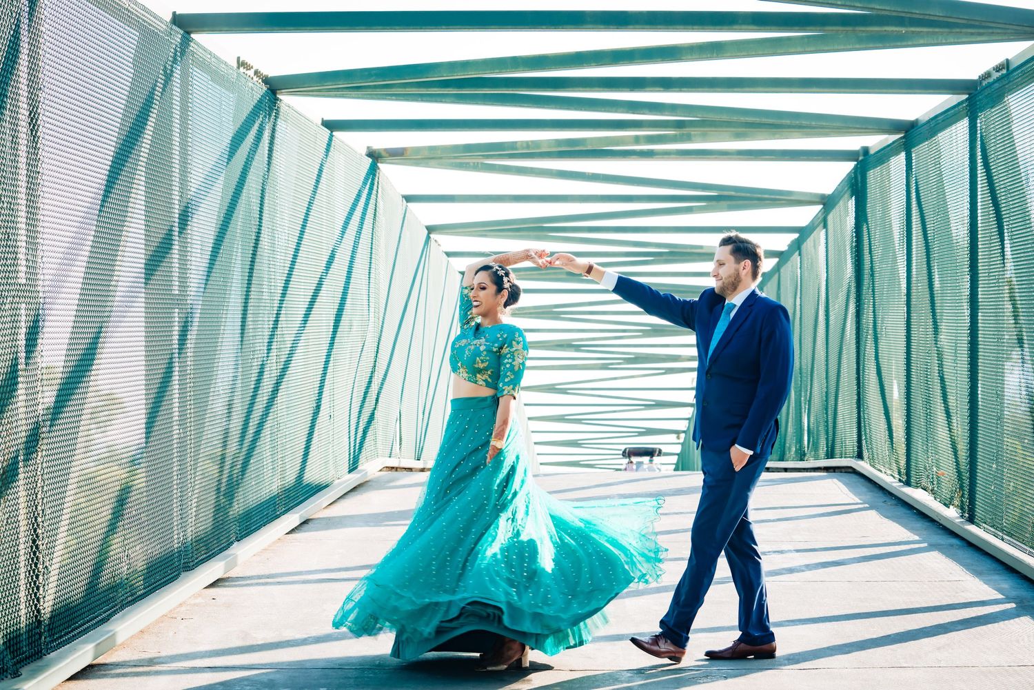 A couple walks through a modern glass corridor with teal-tinted windows creating geometric reflections and patterns.