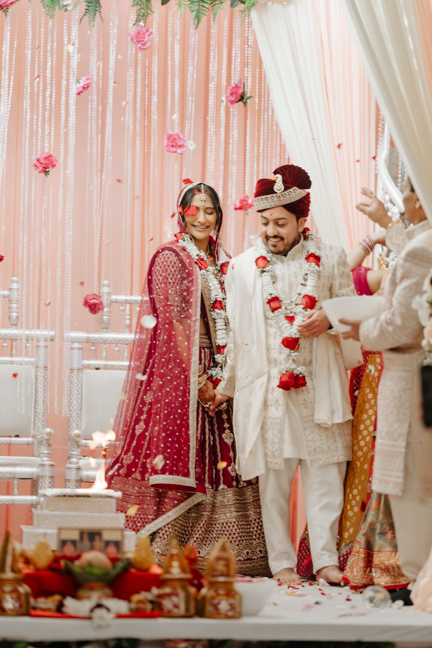 Traditional Indian wedding ceremony with rose petals falling and elegant red and white decor.