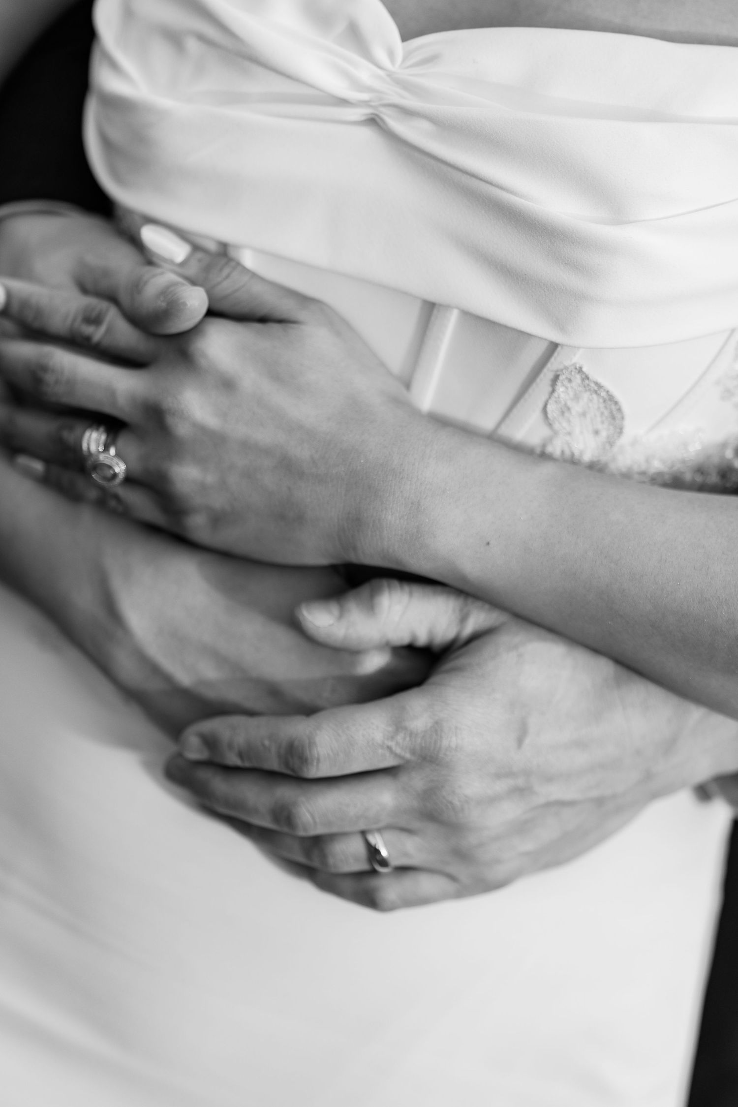 Black and white photo of a couple embracing, showing wedding rings on their hands.