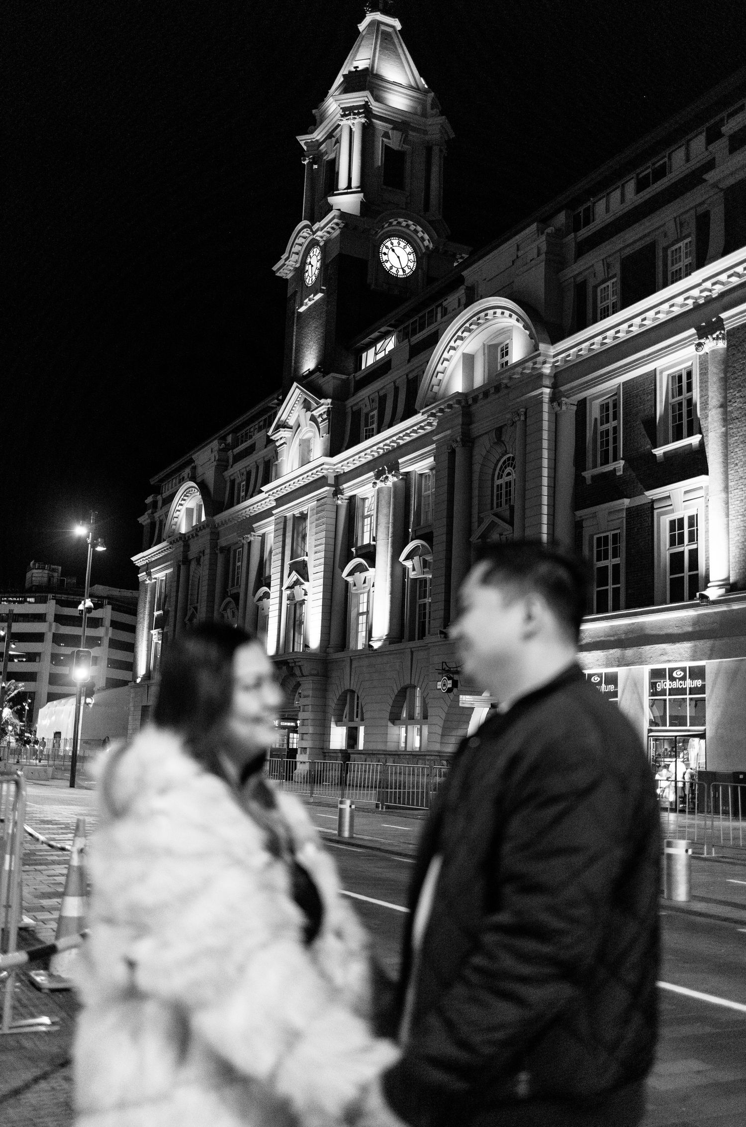 A dramatic black and white photo in front of an illuminated historic clock tower at night.