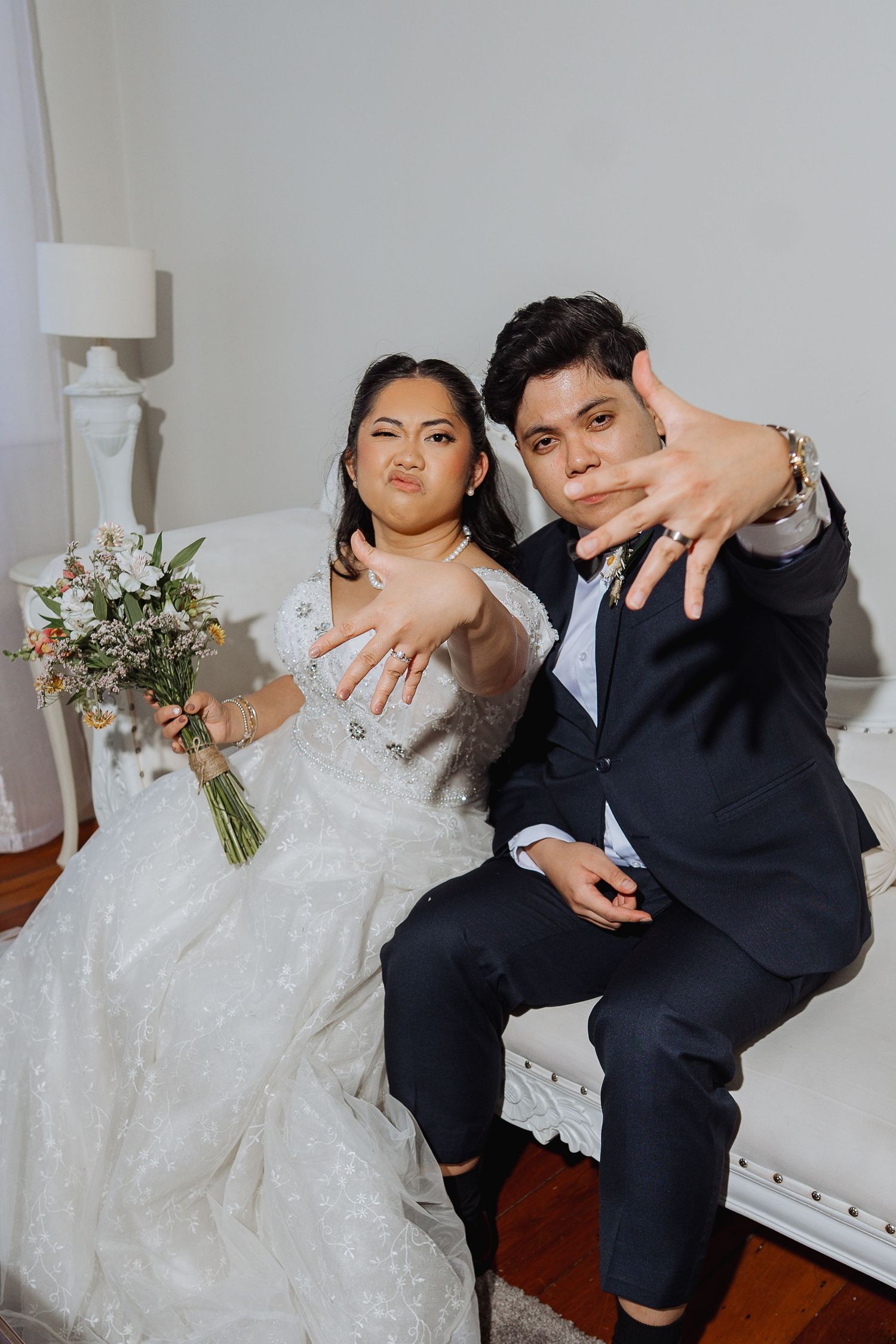 A playful wedding couple poses together in a white studio setting showing off their rings.