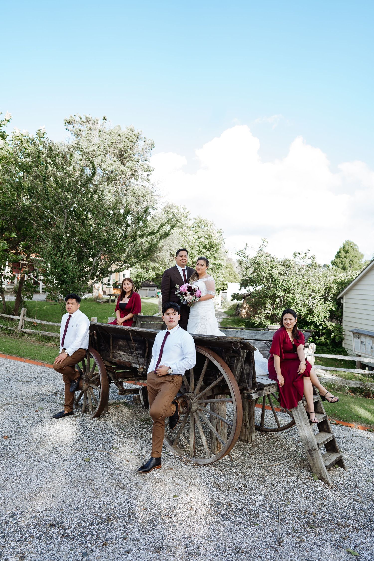 Wedding party members posing on vintage wooden wagons in a rustic outdoor setting.