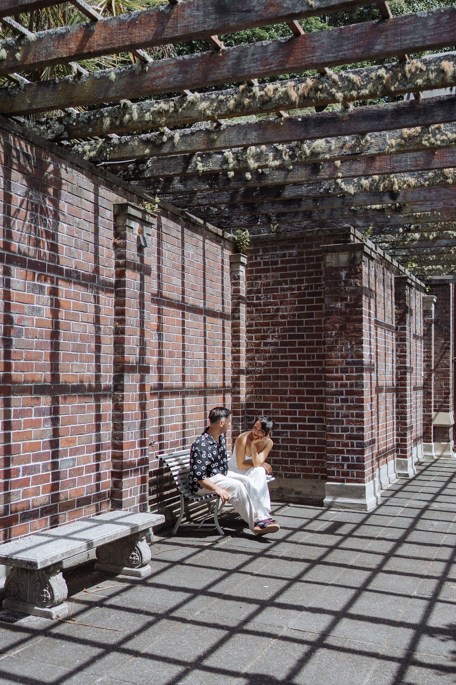 A covered brick walkway with geometric shadow patterns cast by overhead pergola.