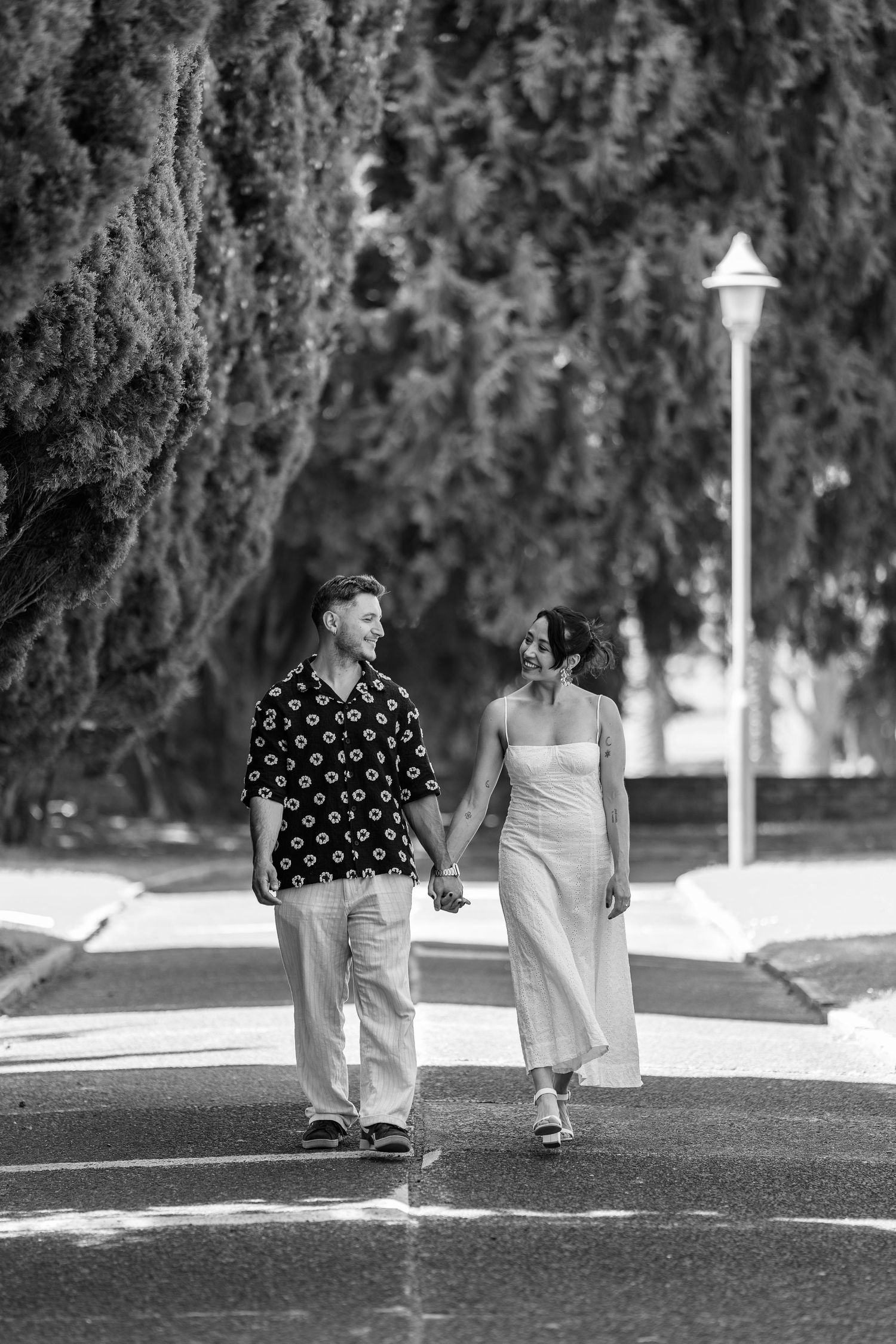 A couple takes a stroll together on a tree-lined path in black and white.