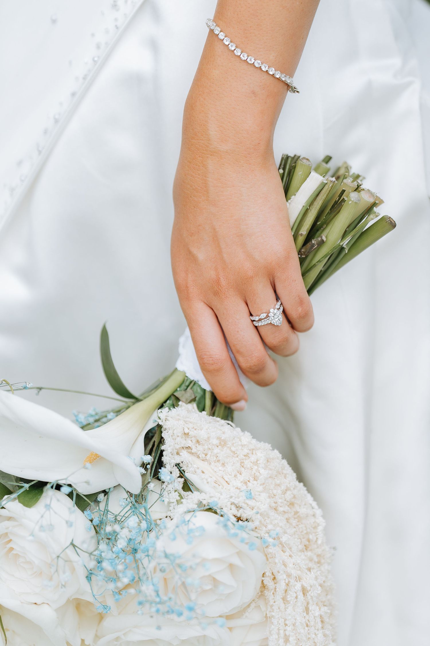Close-up of hands holding a white and light blue wedding bouquet against a white dress.
