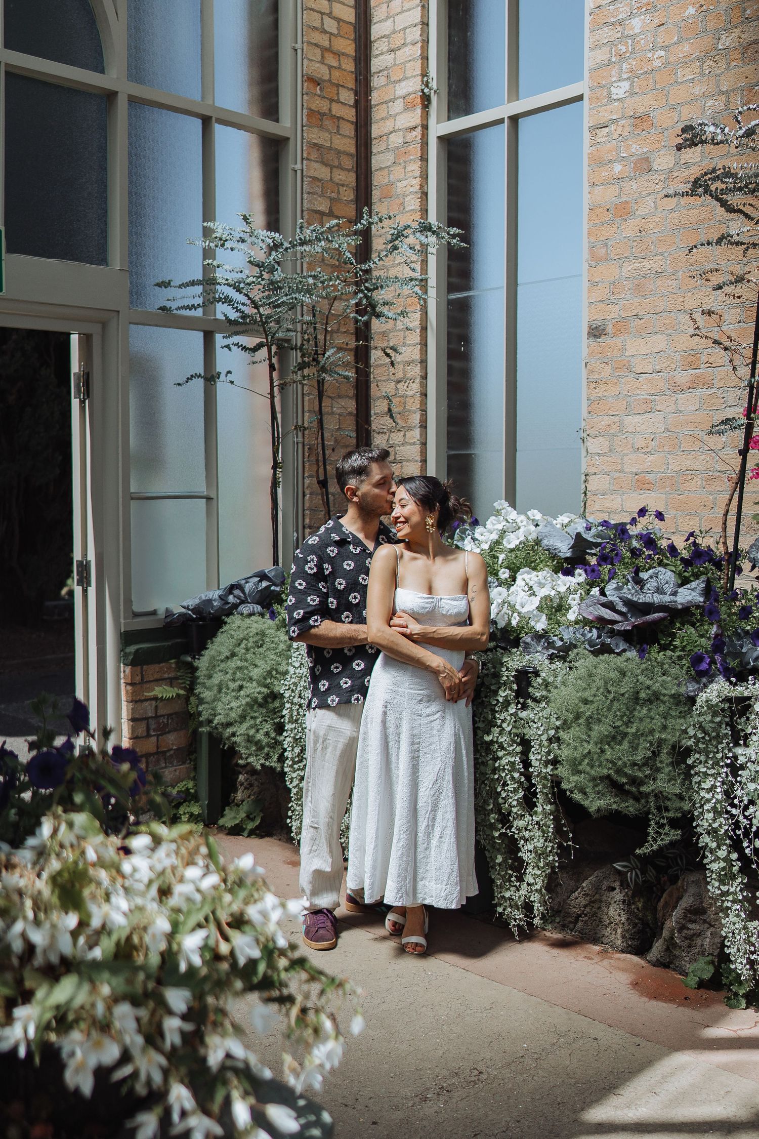 A romantic moment captured outside a brick building with decorative garden planters.