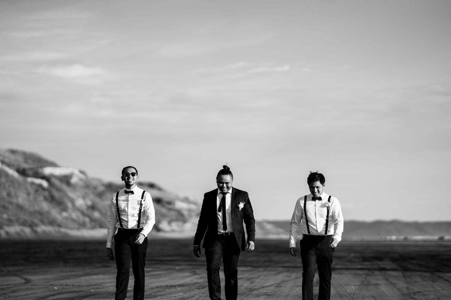 Three people in formal attire walk together on a road with mountains in the background in black and white.