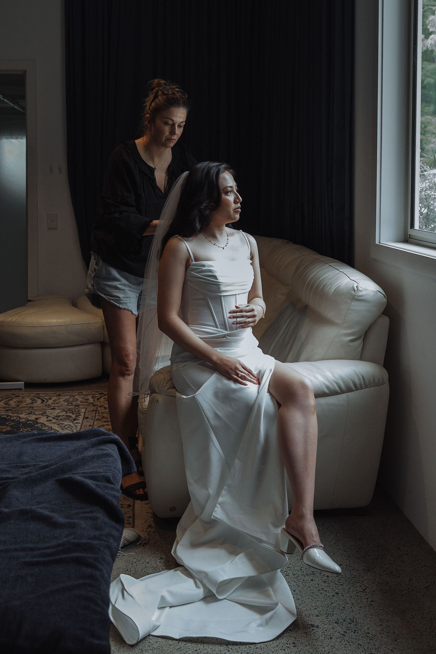 Wedding preparation scene in moody lighting with white dress near window.
