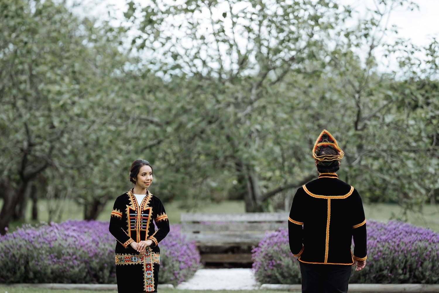 Traditional cultural wedding attire photographed in a garden with lavender and flowering trees.