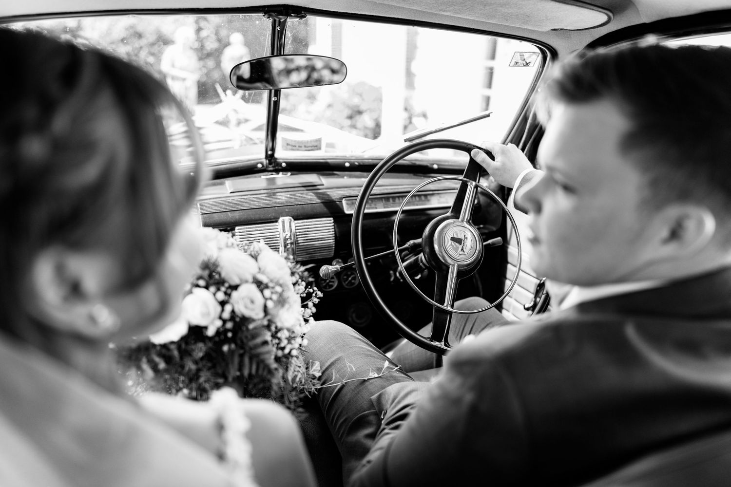 Interior view of vintage car dashboard and steering wheel in black and white.