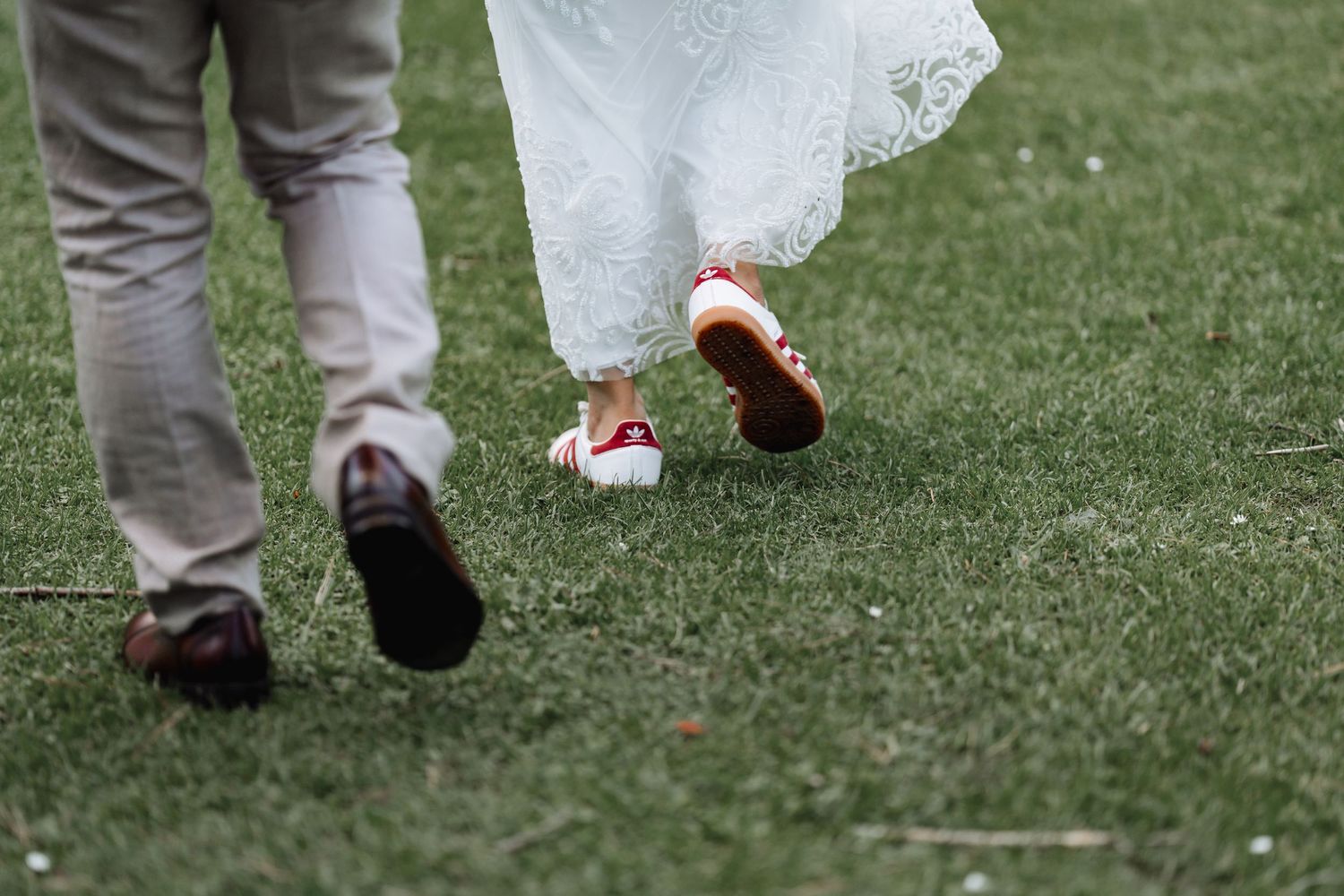 Close-up of couple's feet walking on grass, bride wearing red sneakers with wedding dress.