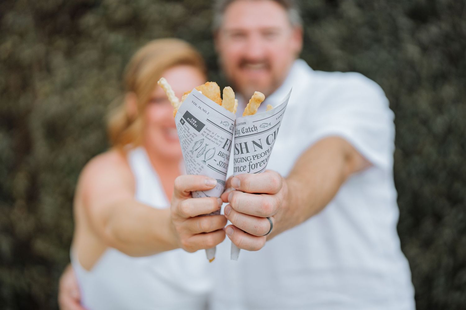 A couple holding hands and exchanging rings during an outdoor wedding ceremony.