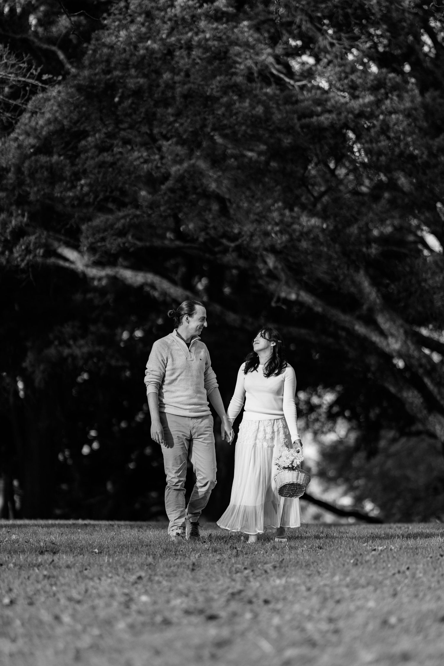 A couple takes a romantic stroll through a park in black and white.