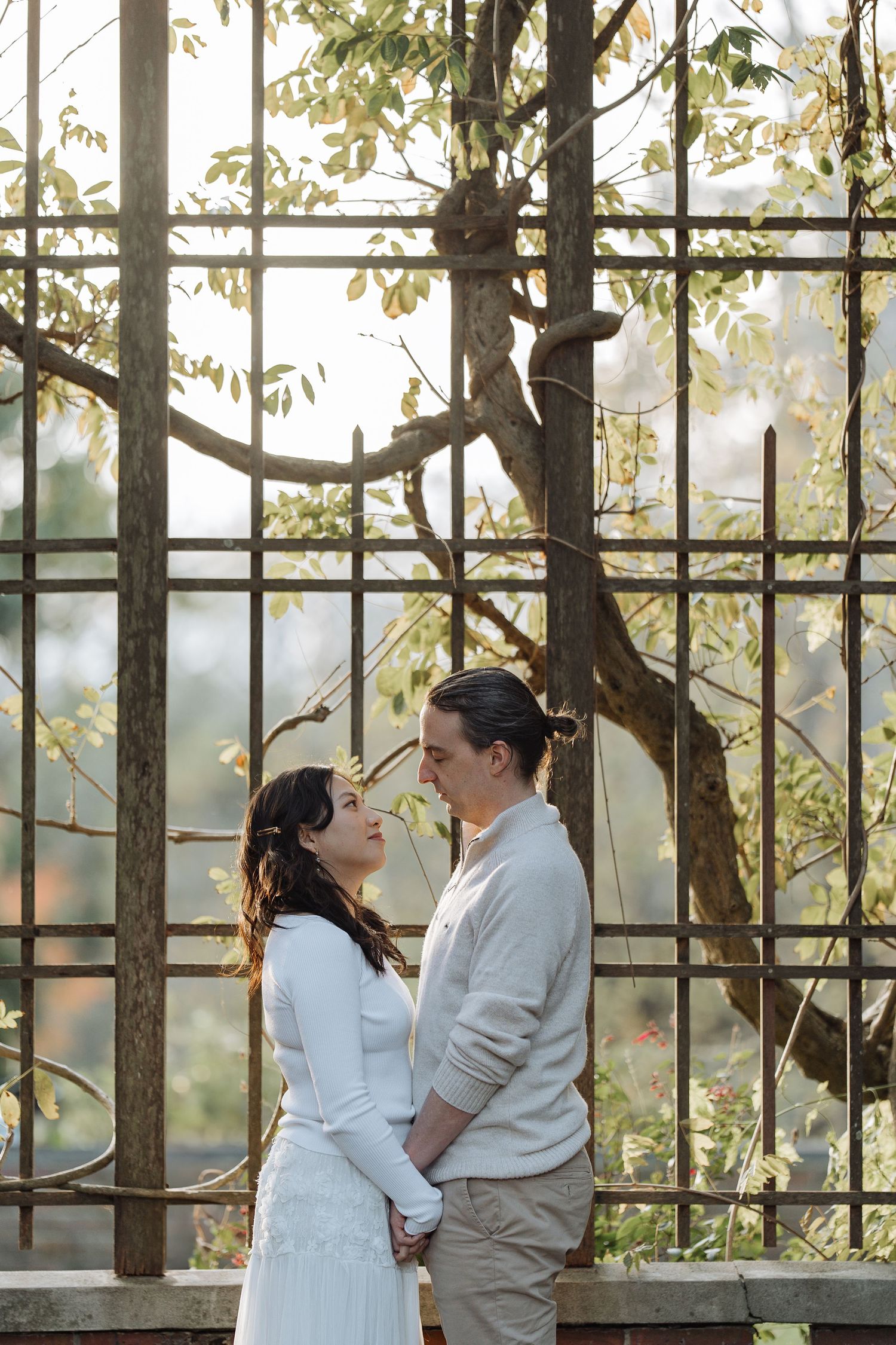 A couple poses together against a latticed garden wall with climbing vines.