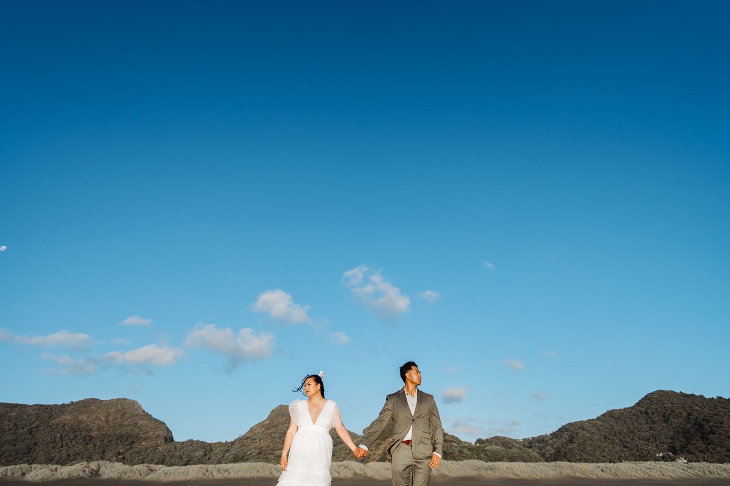 Wedding couple poses against dramatic coastal landscape with blue sky.