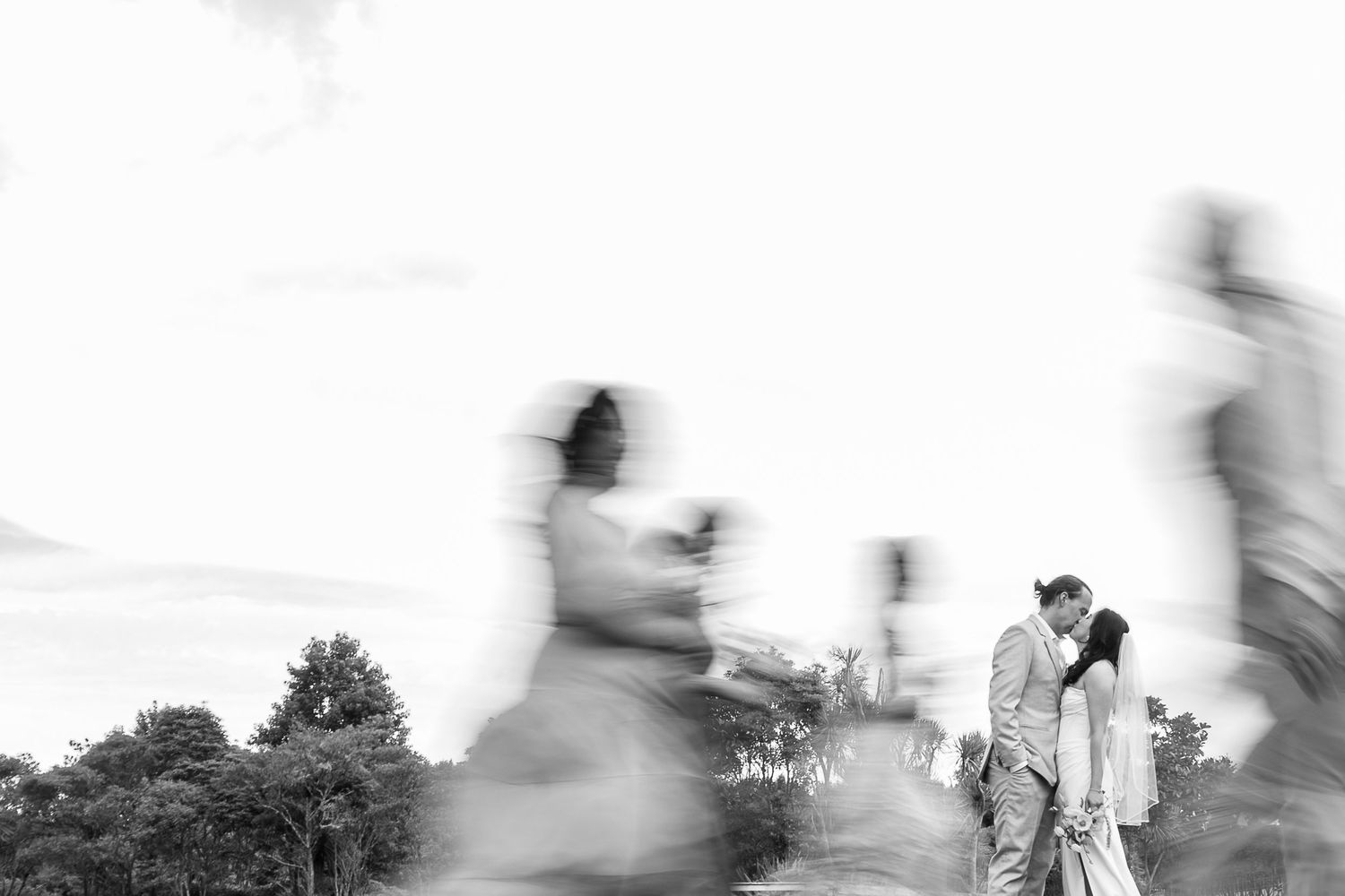 Black and white motion blur photo of people walking in a park with a couple standing still in the background.