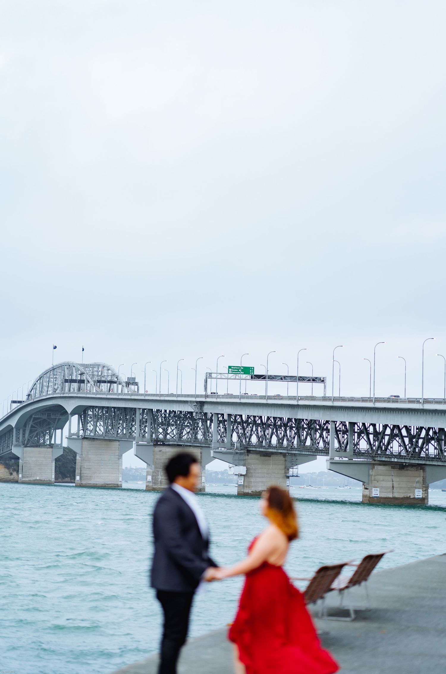 Couple poses near harbor bridge in romantic seaside photoshoot.