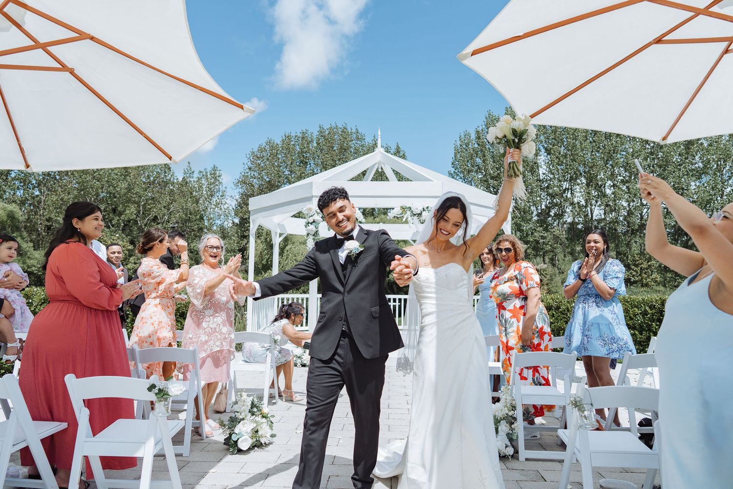 Wedding celebration under white umbrellas with guests dancing and celebrating.
