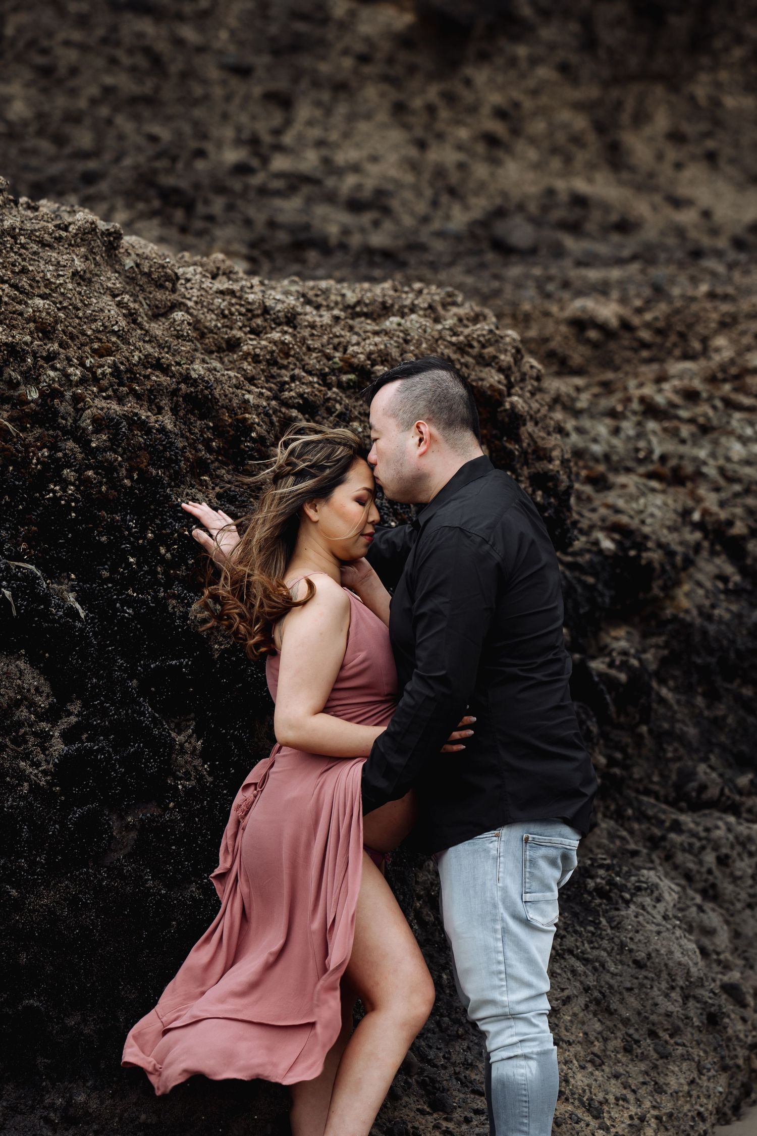 An intimate couple's portrait against dark volcanic rocks at the beach.