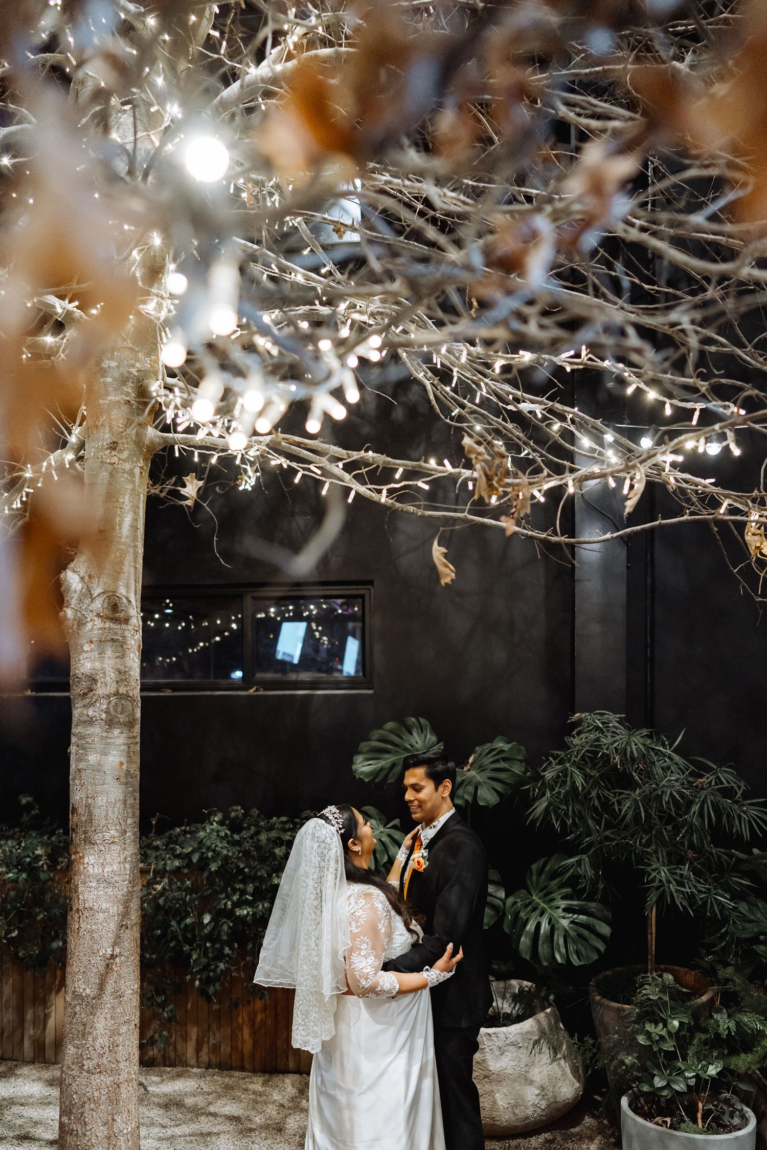 A romantic moment captured under twinkling lights and bare winter branches at an evening wedding venue.