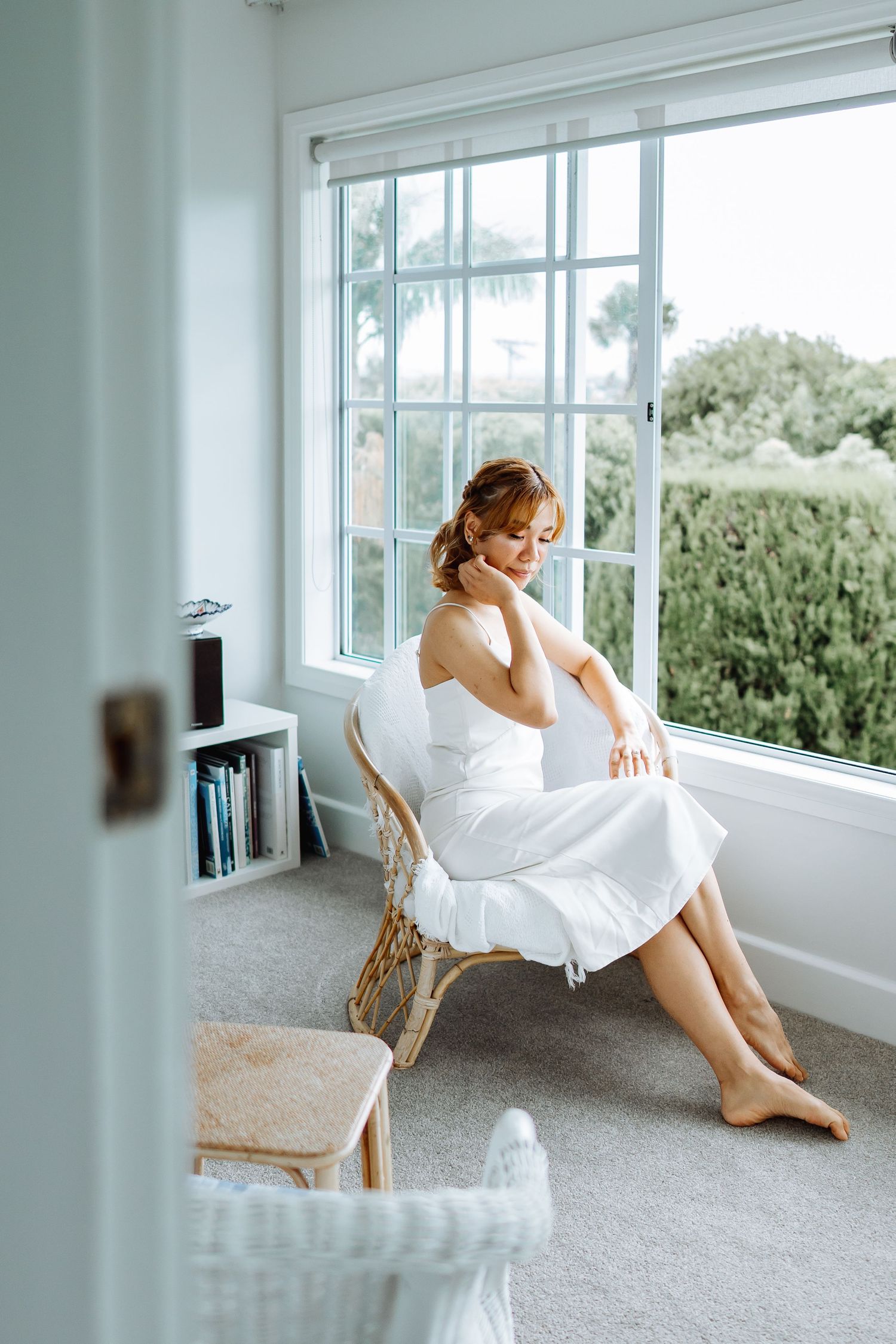 A bright sunlit room with white decor and large windows overlooking green foliage.