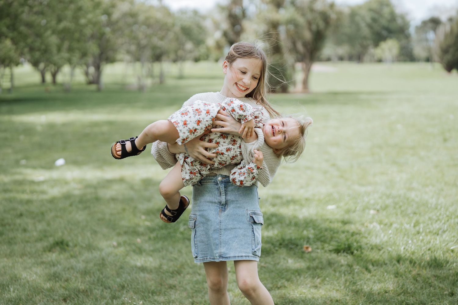 A playful moment as one child carries another horizontally in a grassy field.