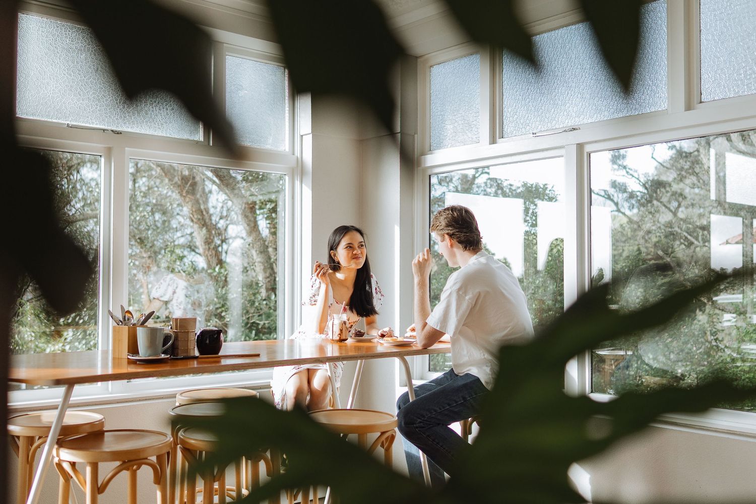 Candid cafe scene through window with natural lighting and wooden furniture.