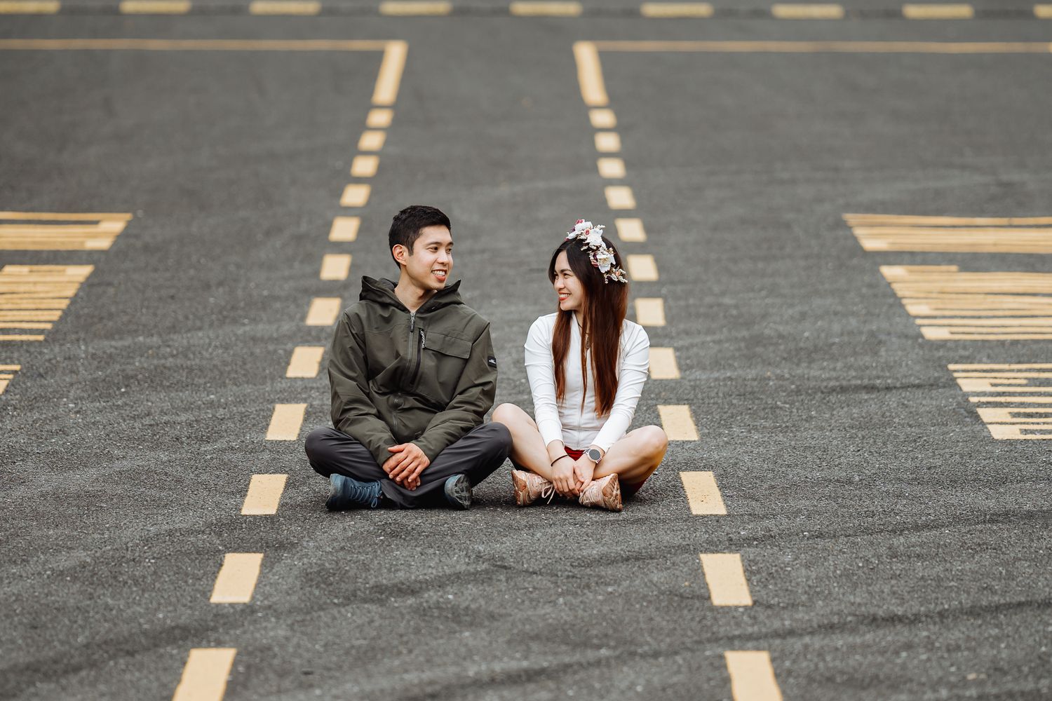 A couple lies on a patterned asphalt surface with yellow road markings.