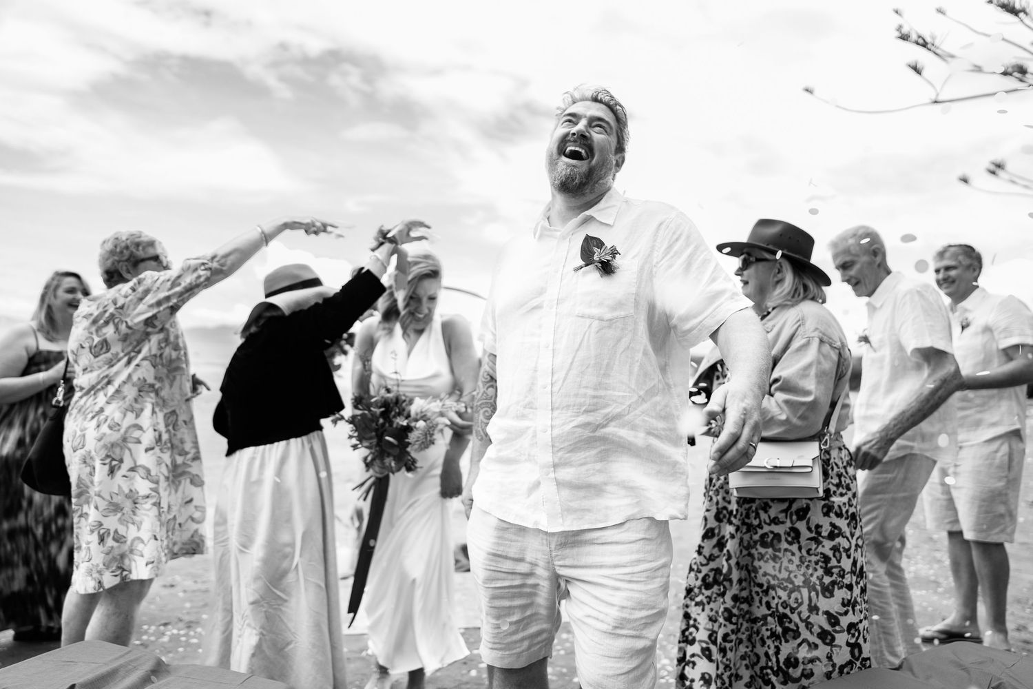 A joyful outdoor celebration captured in black and white with people laughing and gesturing during a wedding ceremony.
