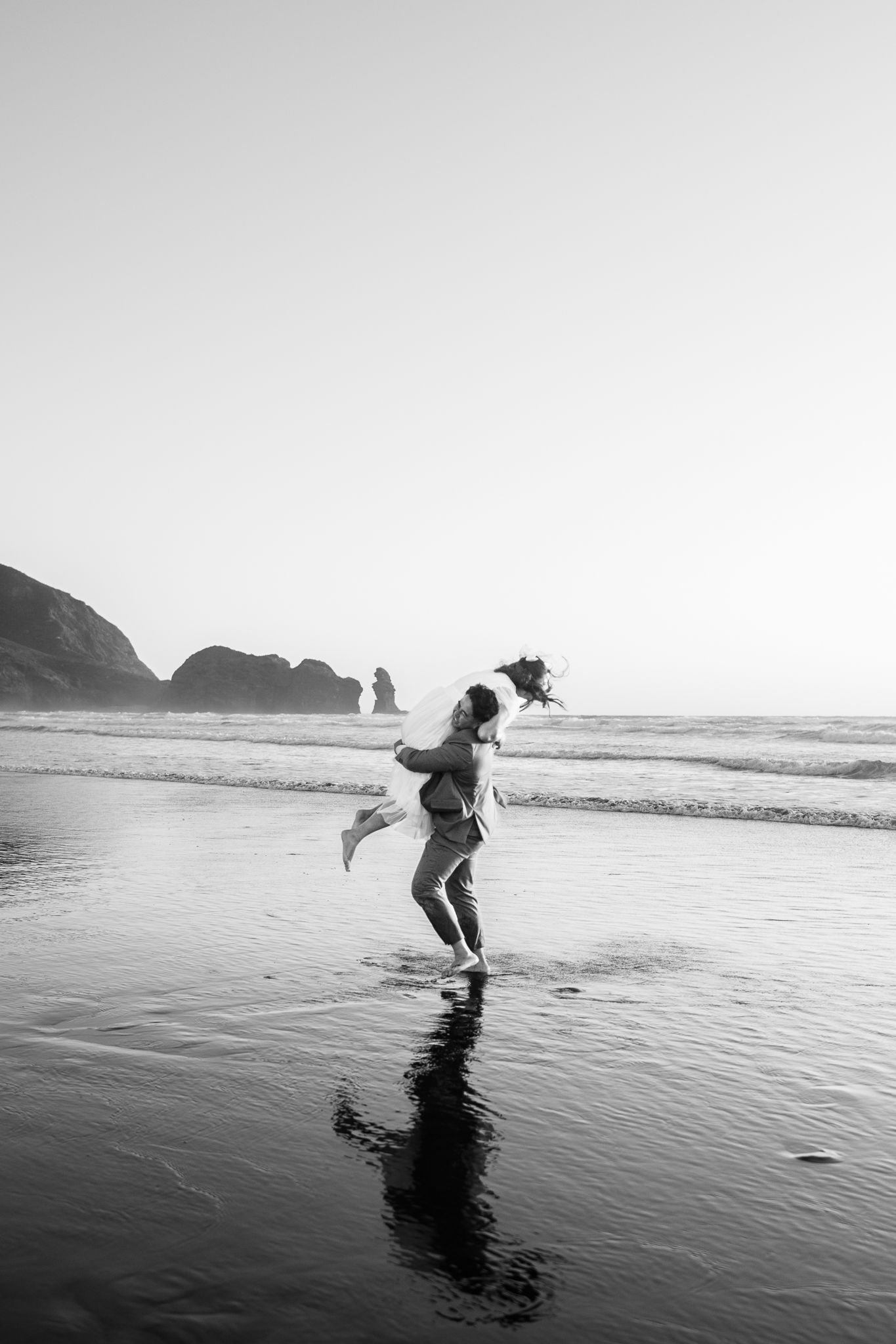 Black and white photo of joyful moment on beach with coastal cliffs in background.